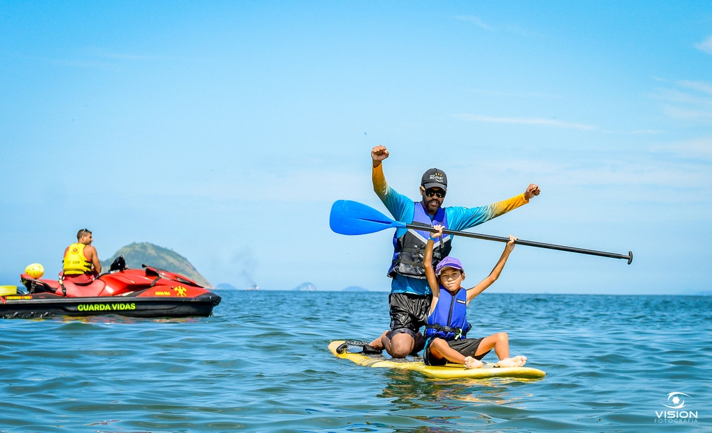 Pai e filho sorrindo em cima de uma prancha de stand up paddle no mar